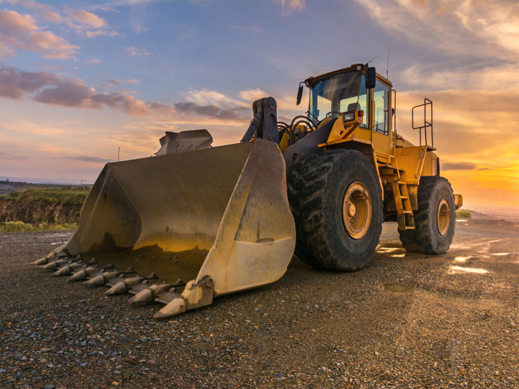 Large front-end loader parked on gravel at sunrise, symbolizing heavy equipment used in construction or agriculture.
